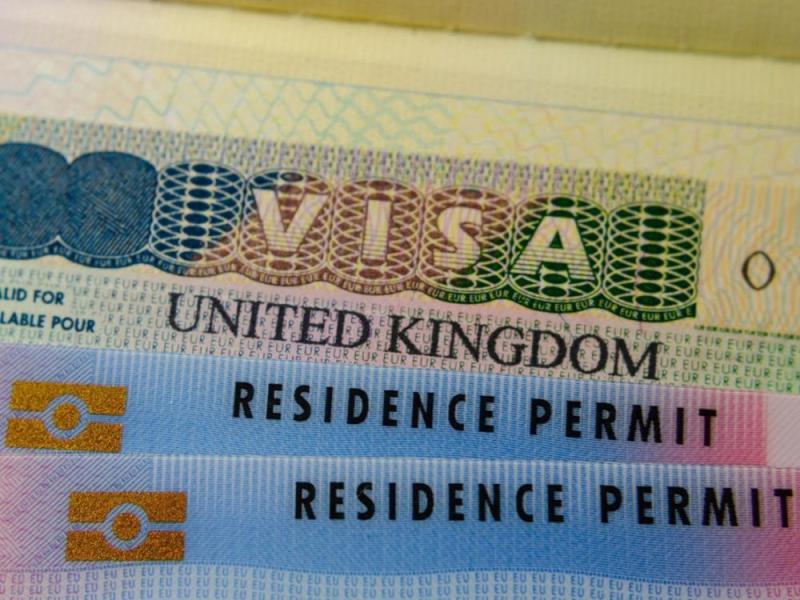 UK BRP cards for Tier 2 work visa placed on top of UK Business VISA sticker in the passport. Close up photo.